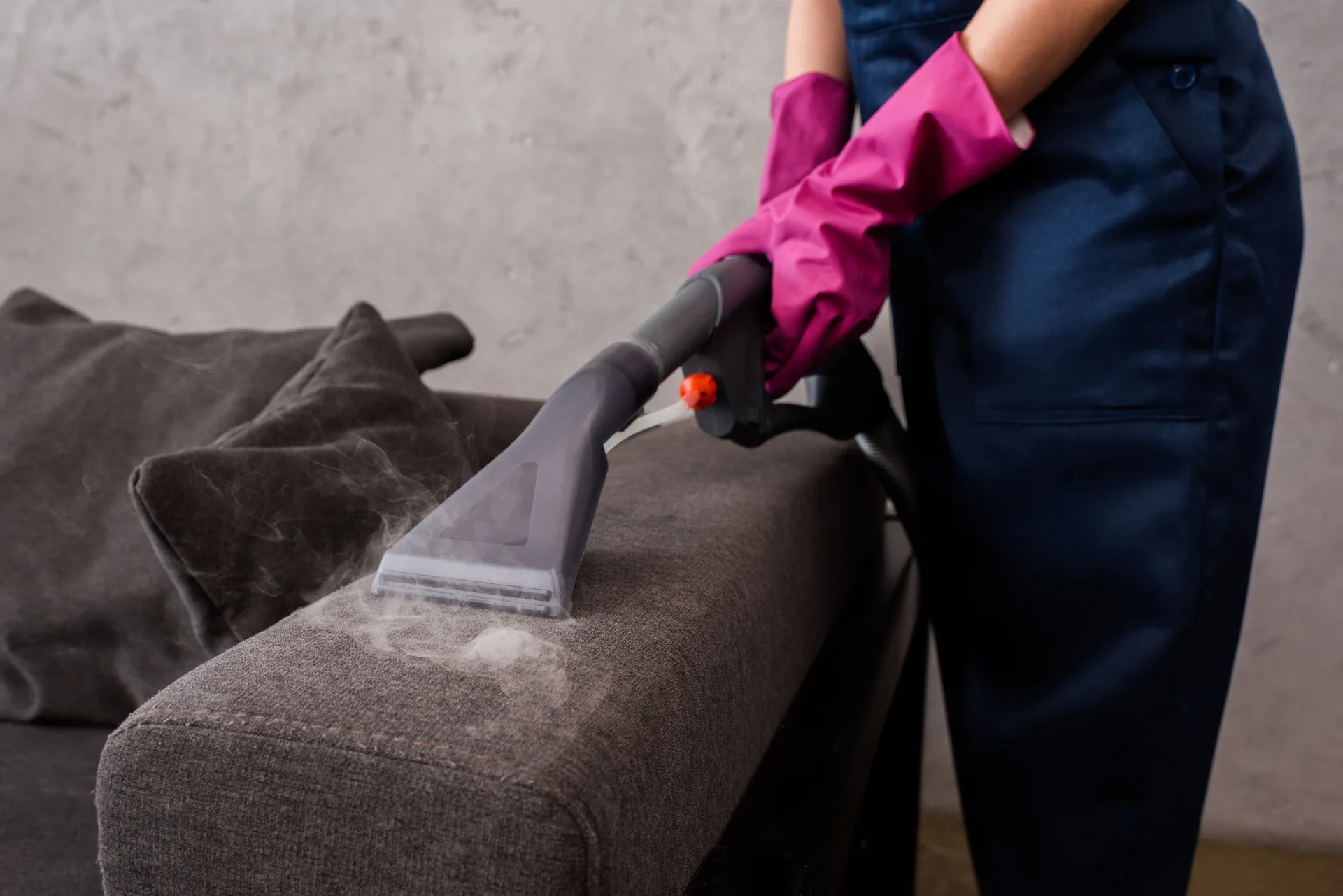 Someone in work uniform running an upholstery cleaner across a sofa