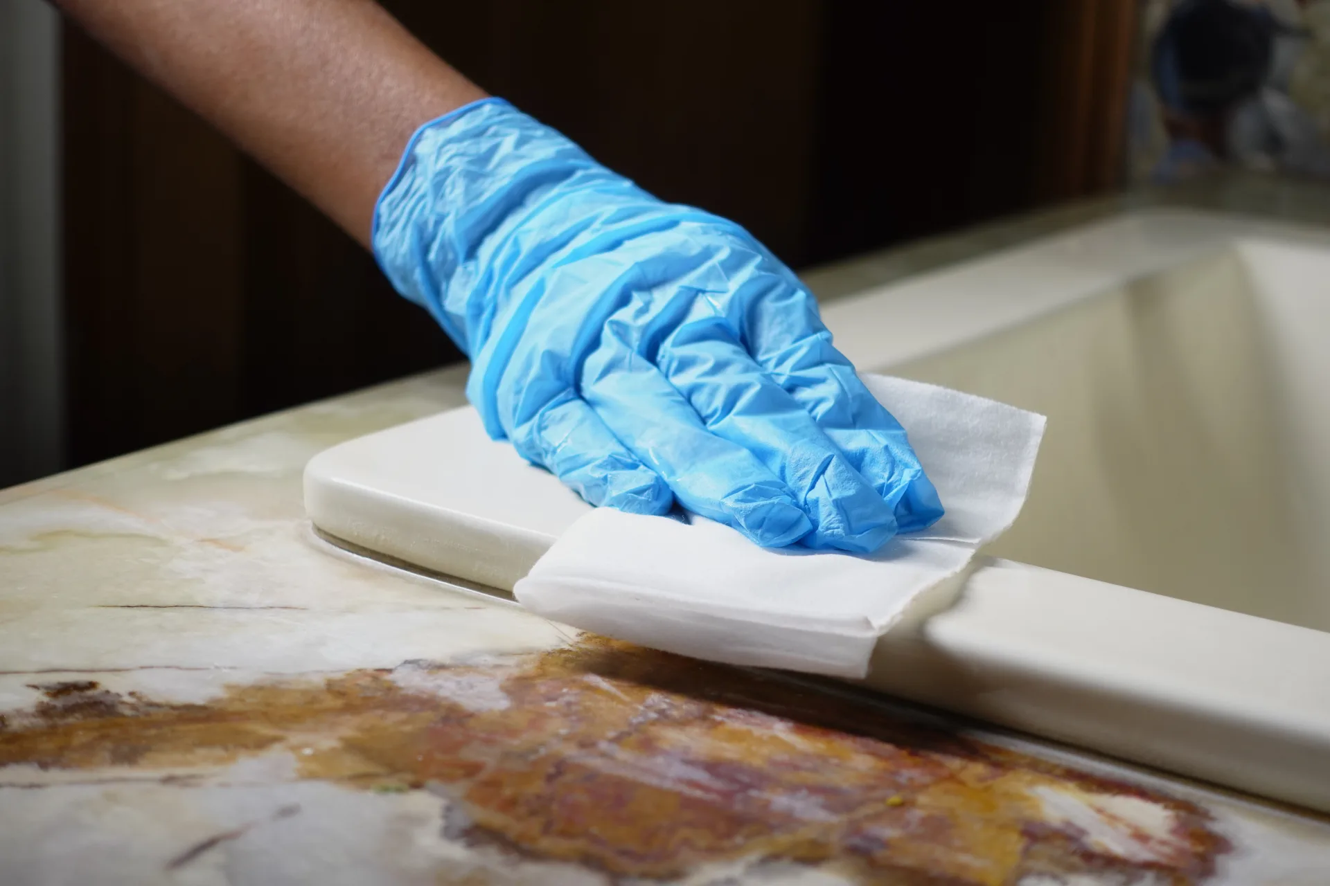 A gloved hand wiping a marble surface with a disposable cloth