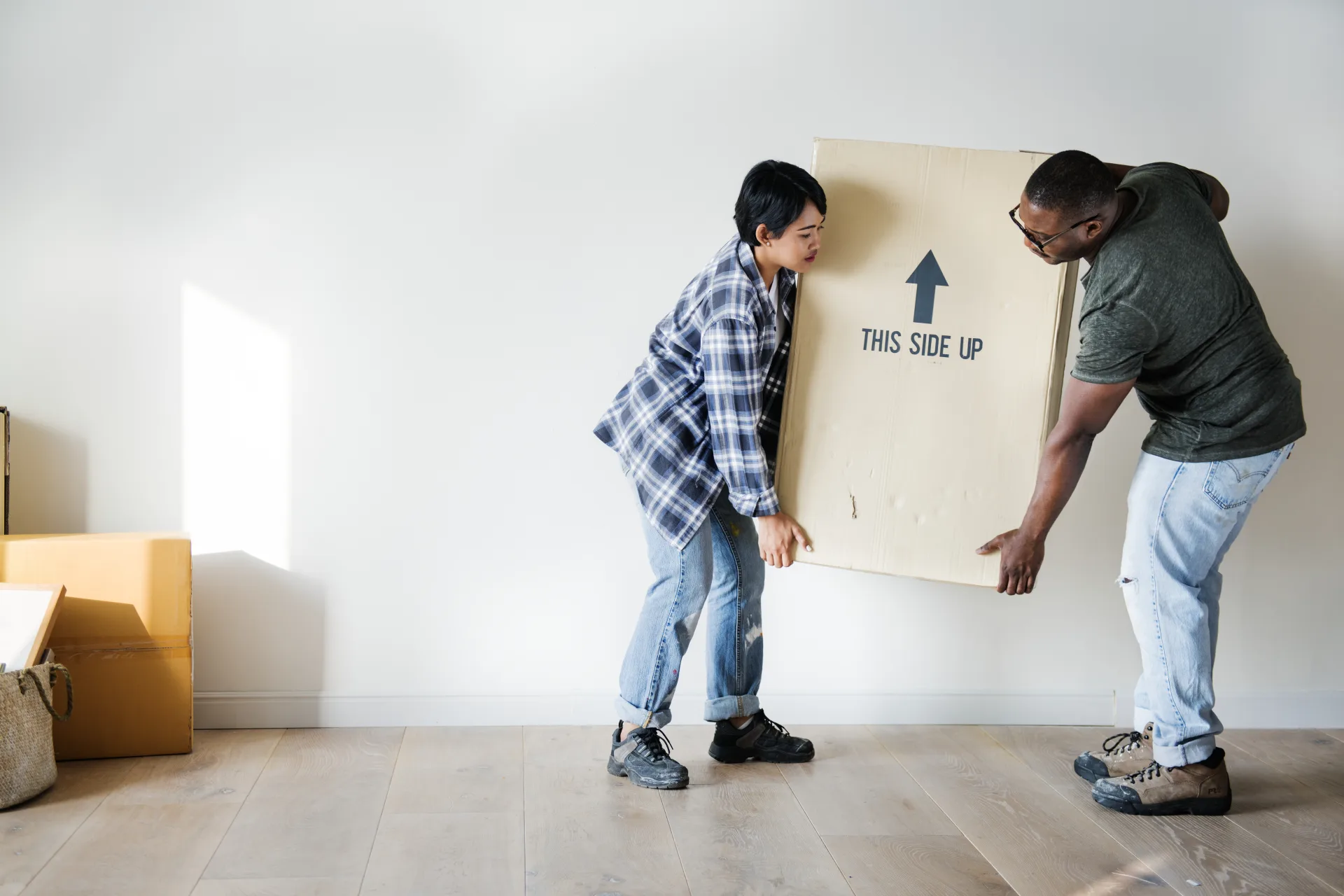 Two people carrying a packing box into an empty room