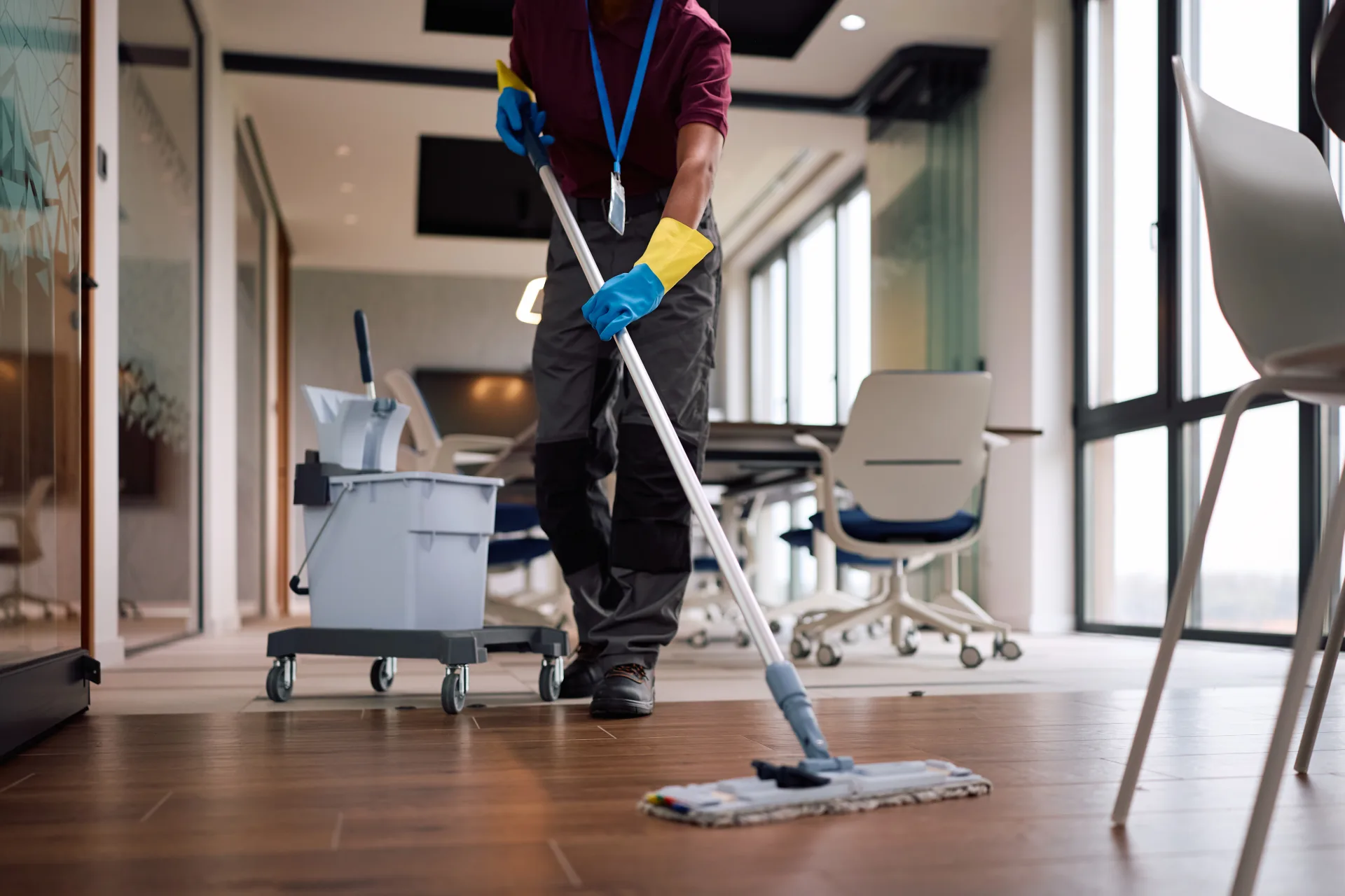 A cleaner mopping the wood floor of an office, desks and chairs to one side