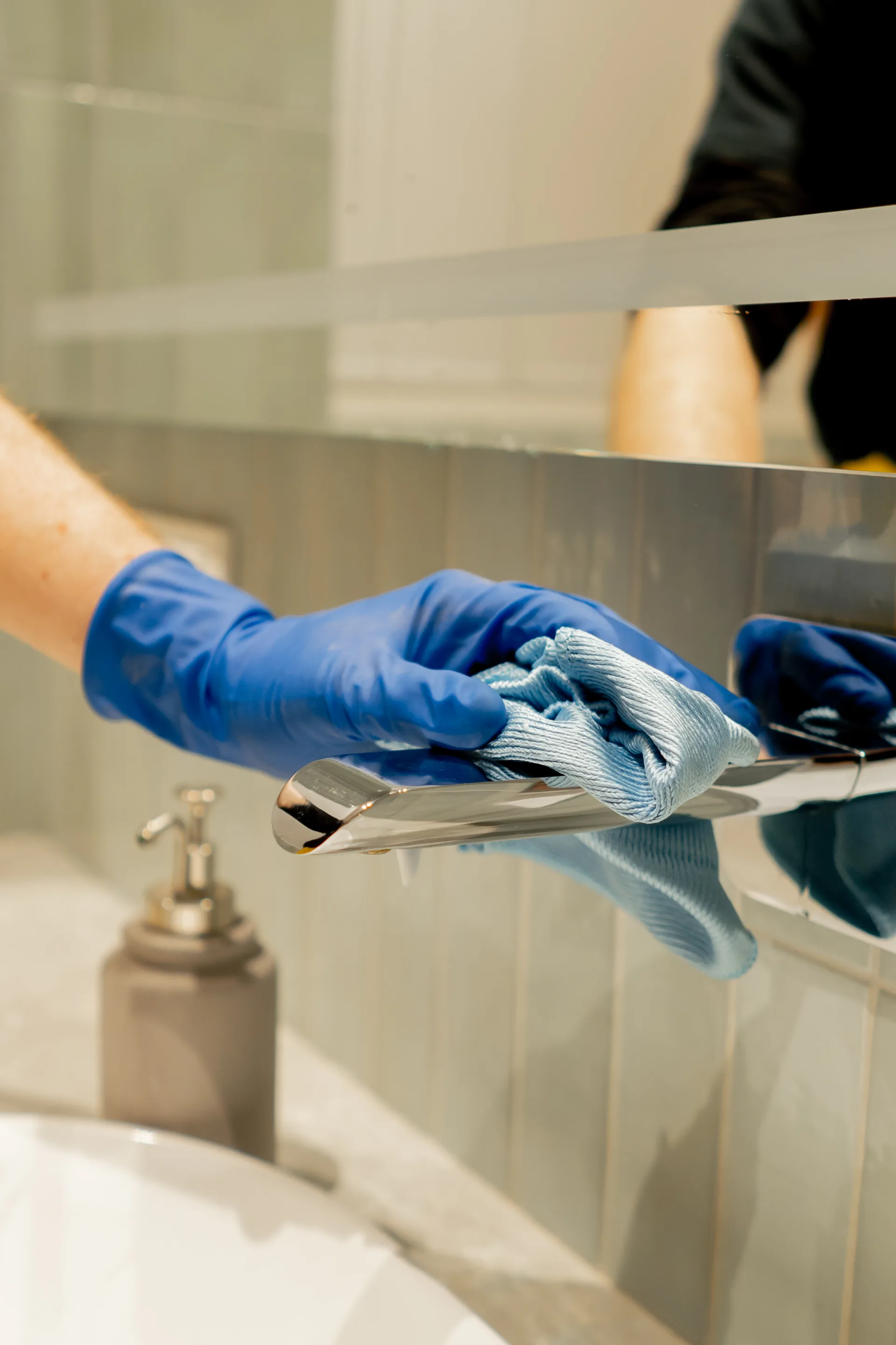 A gloved hand wiping down a bathroom tap with a microfibre cloth